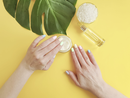 female hands manicure, cosmetic cream, monstera leaf, yellow backgroundの写真素材