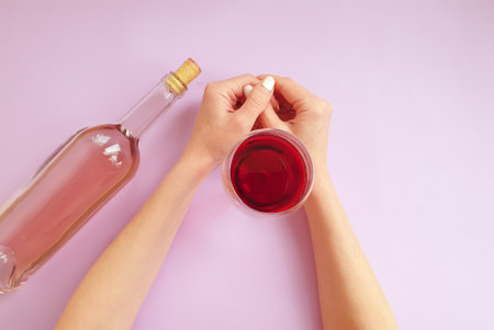 female hands holding a glass of wine on a colored backgroundの写真素材
