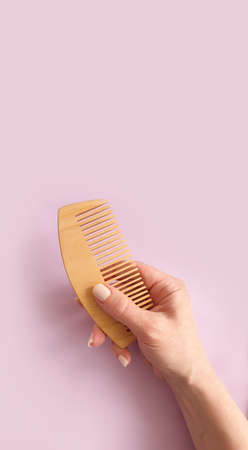 female hand holding a wooden comb on a colored backgroundの写真素材