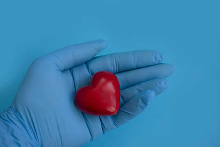 hand in a medical glove holds a heartの写真素材