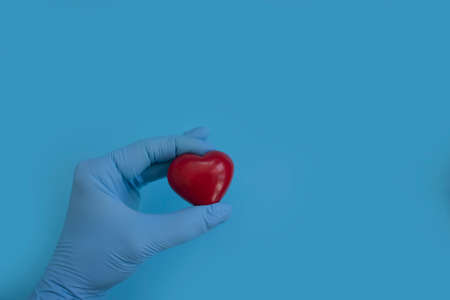 hand in a medical glove holds a heartの写真素材