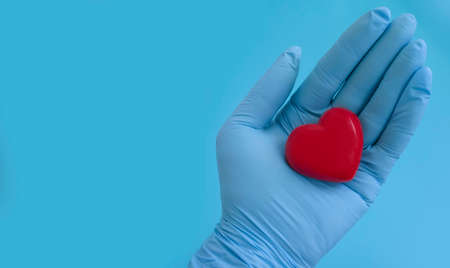 hand in a medical glove holds a heartの写真素材