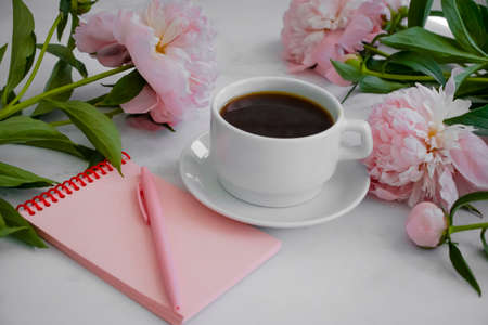 Cup of coffee, peony flower, notebook on a light backgroundの写真素材