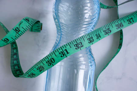 Bottle of water centimeter tape on a light background