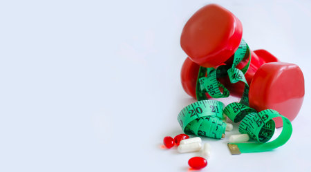 Dumbbells, measuring tape, capsules on a light background