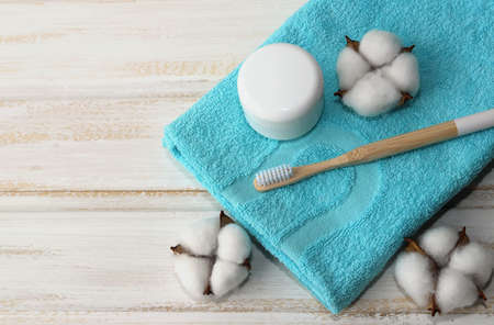 A wooden toothbrush , a jar of tooth powder, and cotton flowers lie on a folded blue soft towel on a wooden white background. Oral hygiene. Selective focus. Zero waste. Top viewの写真素材