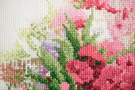 Colorful fragment of a cross-stitch embroidery with pink flowers.