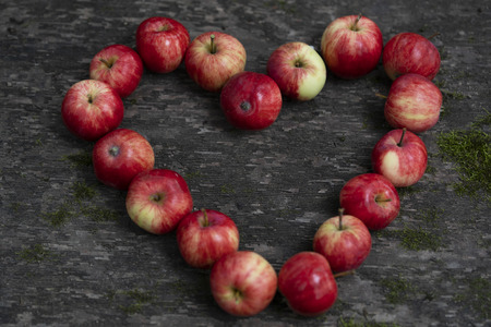 Heart-shaped red apples on an old wooden surface  covered with moss here and there. Heart-shaped red apples on an dark old wooden table.の写真素材