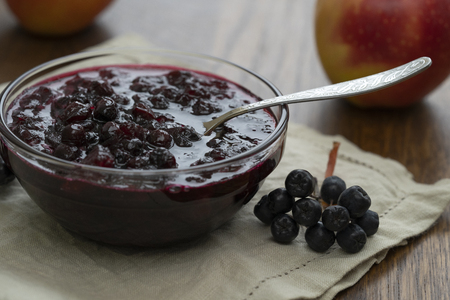 Home made black chokeberry and apple confiture in a glass jar on a wooden background.の写真素材