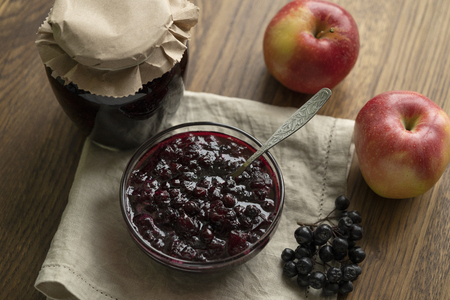 Home made black chokeberry and apple confiture in a glass jar on a wooden background.の写真素材