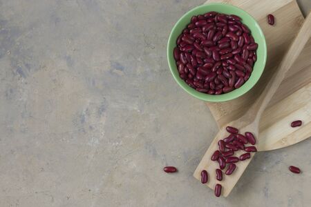 Legumes on a light background. Red bean in a green bowl with a wooden spoon on a wooden board. Healthy food for vegans. Horizontal position. Top view. Copy spaceの写真素材