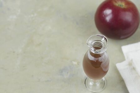 Apple cider vinegar in a glass bottle and a fresh red apple on a light background. Cotton textile....