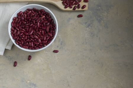 Legumes on a light background. Red bean in a light bowl with a wooden spoon. Healthy food for vegans. Horizontal position. Top view. Copy spaceの写真素材
