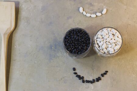 Beans on a light background. Black beans and white beans in a glass bowl with a wooden spoon. Healthy food for vegans. Horizontal position. Top view.の写真素材