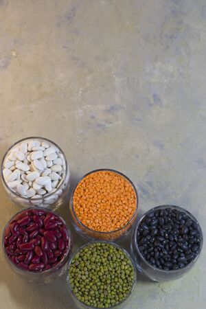 Legumes on a light background. Red beans, black beans, white beans, lentils and mung bean in a glass bowl. Healthy food for vegans. Vertical position. Top view. Copy spaceの写真素材