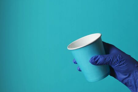 Paper cup in a woman's hand on a blue background. Virus protection. Ecological tableware for drinks....