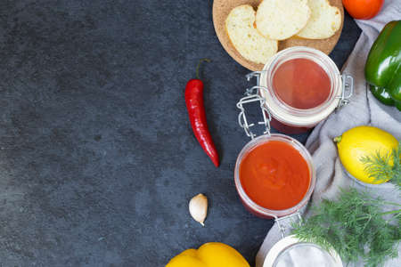 Aivar caviar in a glass jar and ingredients for it - sweet pepper, tomatoes, garlic, hot pepper, dill on a dark background. Sliced bread for snacks. Vegetarian food. Copy space.の写真素材