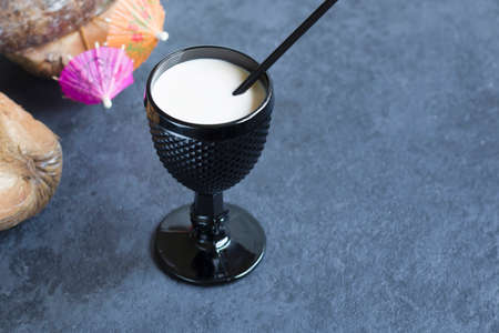 Non-alcoholic coconut milk cocktail in a black glass. Cocktail umbrellas and coconut fruits. Copy spaceの写真素材