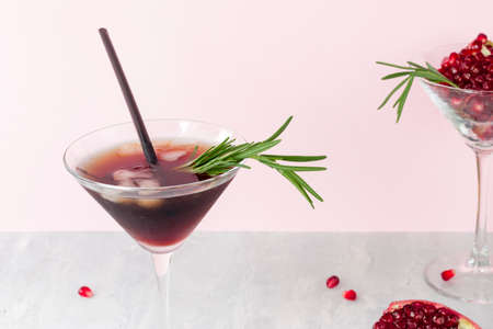 Cold non-alcoholic pomegranate cocktail with rosemary on a light pink background. Fruit grains in a glass. Natural healthy drink.の写真素材