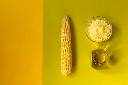 Corn oil and flour in a glass bowl, fresh corn on a double yellow green background. The concept of...