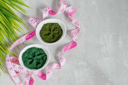 Chlorella and spirulina powder on a light background. A green superfood detox for a vegetarian diet. Healthy lifestyle concept. Measuring tape for the figure. Copy space.の写真素材