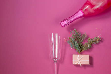 Festive New Year concept. A bottle of pink champagne and a glass for it on a pink background. Christmas tree, garland and gift box. Copy space. Postcard top view. flat layの写真素材