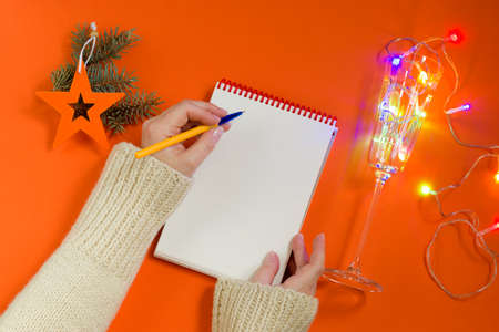 Christmas composition: Christmas tree decorations, garland, notebook and pen on an orange...