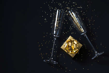 Gift box and two glasses, golden confetti on a festive black background. Festive Christmas, New Year concept. Copy spaceの写真素材
