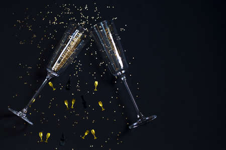 Two champagne glasses, golden confetti on a festive black background. Festive Christmas, New Year concept. Copy spaceの写真素材