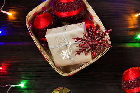 Christmas gift boxes in a natural basket with red Christmas balls and snowflakes on a dark wooden...