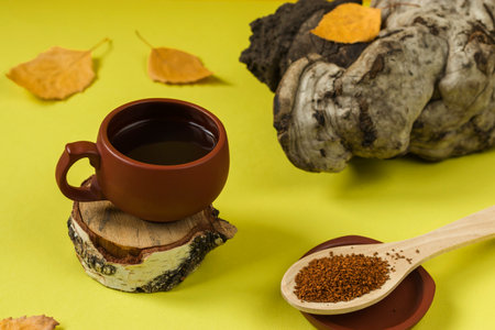 Healing pieces of birch chaga in a wooden spoon on a yellow background. Birch mushroom tea in a...