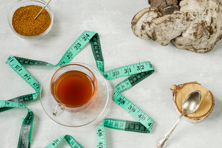 Chaga birch mushroom is a trendy superfood for diet and immunity. Natural tea, coffee and pieces of birch chaga in a glass cup, measuring tape on a light background. Natural antioxidant. View top.の写真素材