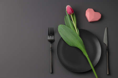 Romantic festive black festive table setting with heart and tulip on a dark background. Valentine's...