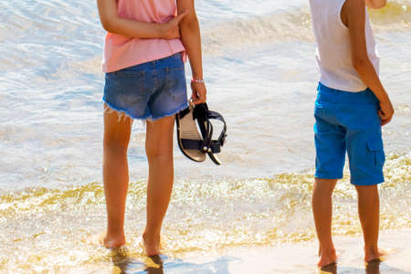 Children's feet are in the water. A boy and a girl enter the sea water. A man tastes sea water with his foot. Summer trip to the sea. Family tourism. Childhood. Healthy lifestyleの写真素材