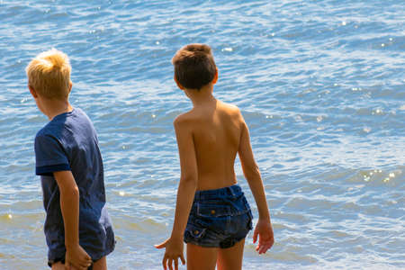 Children's feet are in the water. The boys are entering the sea water. A man tastes sea water with his foot. Summer trip to the sea. Family tourism. Childhood. Healthy lifestyleの写真素材
