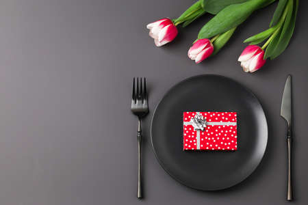 Romantic festive black holiday table setting with gift box and tulip on dark background. Valentine's...
