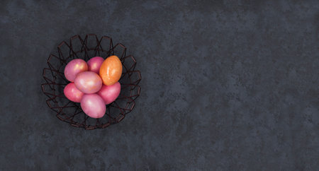Concept of Easter holiday and spring. Banner. Easter multicolored pastel pink eggs in a metal basket on a dark background. Flat lay. Minimal style. Copy space.の写真素材