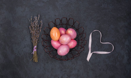 Easter multicolored pink eggs in a metal basket and a heart made of ribbon, a bunch of lavender on a...