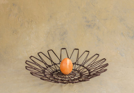 Creative colored orange egg in a metal basket on a light background. Happy easter. Spring holiday...