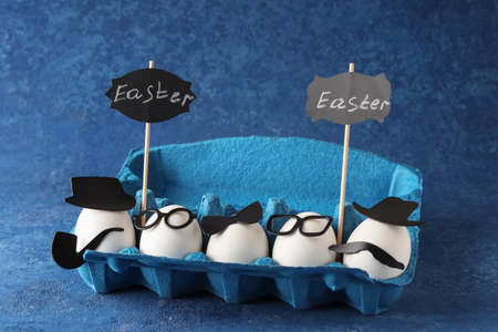 Easter creative holiday concept. White eggs of a chicken farm in a cardboard blue market box on a solid background. Cheerful company of figuresの写真素材