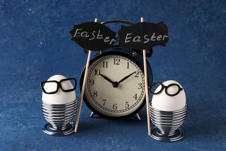 White eggs of a chicken farm on a blue background. Easter creative holiday concept. Glasses and breakfast. Alarm clock and timeの写真素材