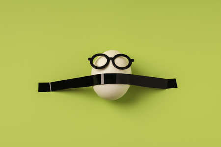 White egg in black glasses on a green background. Creative concept of Easter holiday. Flat layの写真素材