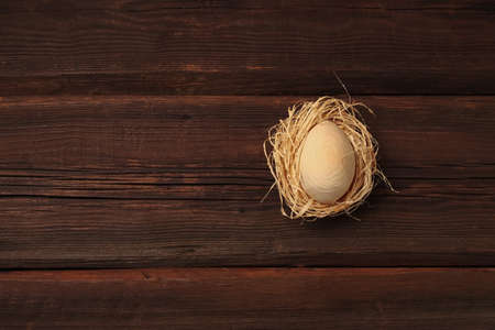 Spring greeting card. Wooden egg in a nest made of hay on a dark natural background. Happy easter concept in eco style. Copy space.の写真素材