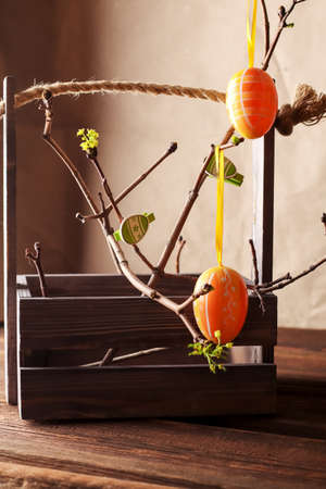 Spring holiday greeting card. Decoration with tree branches, green leaves, eggs on a dark wooden...