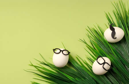 Cheerful creative white eggs on a green background. Creative concept of Easter holiday. Flat lay. Copy spaceの写真素材