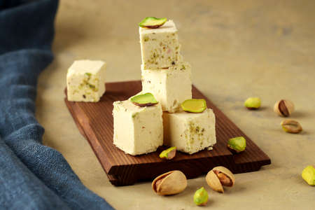 Halva with pistachios on parchment paper on a wooden background. Natural vegan product. Turkish,...
