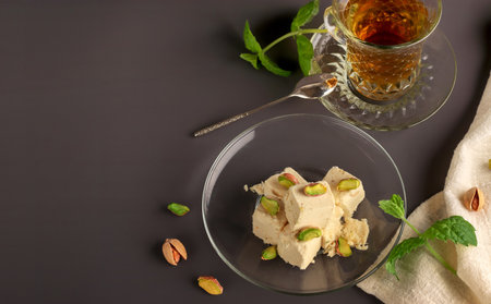 Natural vegan product. Halva with pistachios on a glass plate on a dark background. Turkish, Arab and Jewish national sweets. Traditional oriental dessert Chekme. Copy spaceの写真素材