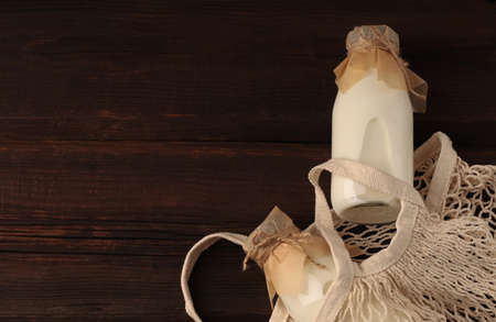 Diet drink for breakfast. Vegetable vegan milk in glass bottles in a string bag on a wooden background. Gluten and lactose free healthy food concept. Copy space, top viewの写真素材