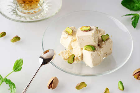 Natural vegan product. Halva with pistachios on a glass plate on a light background. Traditional...