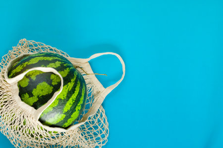 Healthy food delivery concept. Watermelon in a string bag on a blue background. Detox in a reusable eco mesh. Copy spaceの写真素材